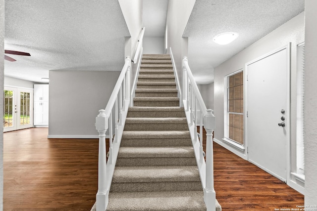 staircase featuring french doors, a ceiling fan, a textured ceiling, wood finished floors, and baseboards