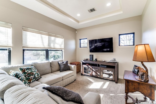 living room featuring a tray ceiling, a healthy amount of sunlight, visible vents, and light carpet