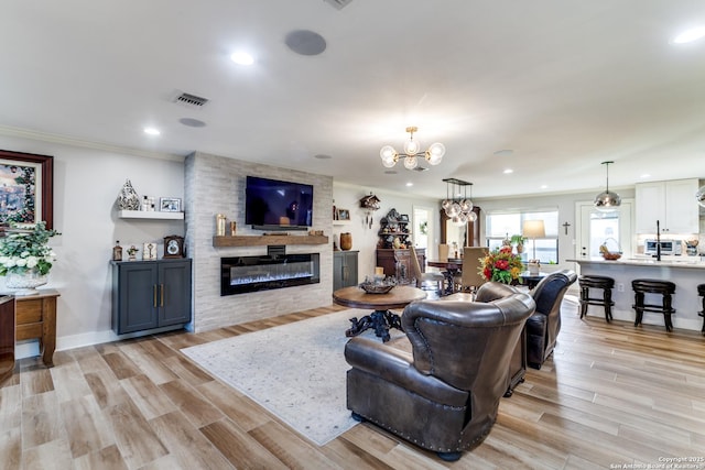 living room with crown molding, a notable chandelier, a fireplace, and light wood-style flooring