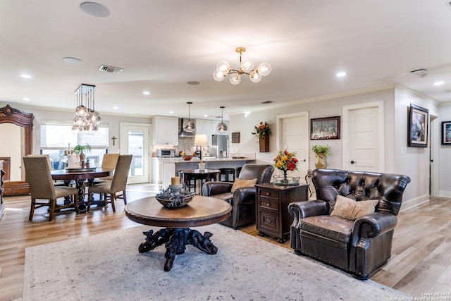 living area featuring light wood-type flooring, visible vents, a chandelier, and crown molding