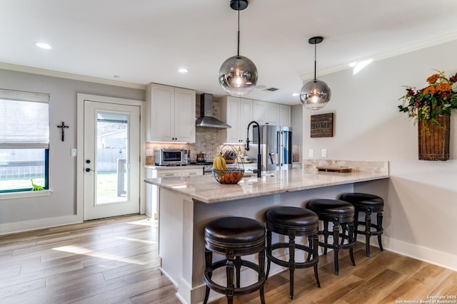 kitchen with light stone counters, a peninsula, a kitchen breakfast bar, wall chimney range hood, and crown molding