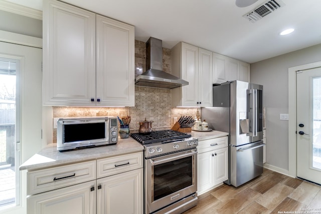 kitchen with stainless steel appliances, wall chimney range hood, visible vents, and white cabinetry