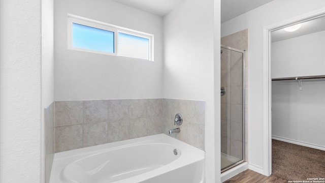 bathroom with wood finished floors, baseboards, a spacious closet, a bath, and a stall shower