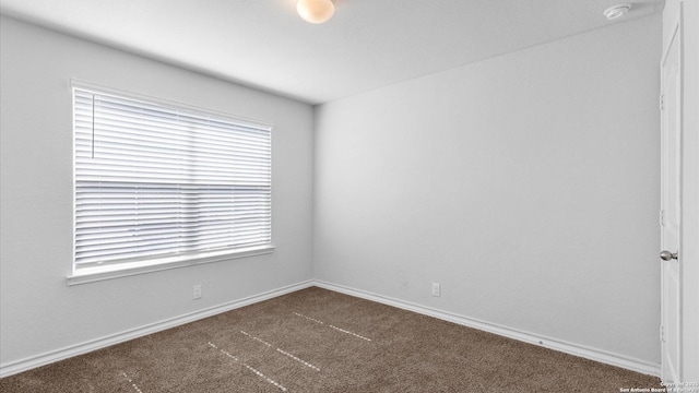 empty room featuring dark colored carpet and baseboards