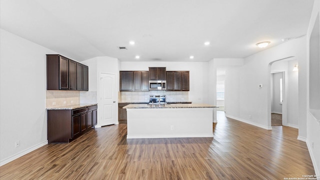 kitchen with light stone countertops, a center island with sink, appliances with stainless steel finishes, and dark wood finished floors