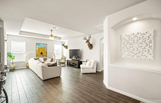 living room with arched walkways, visible vents, baseboards, wood tiled floor, and a tray ceiling