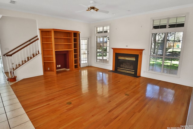 unfurnished living room with a fireplace with flush hearth, stairs, ornamental molding, and wood finished floors