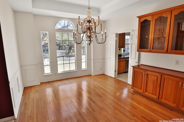 unfurnished dining area featuring a wainscoted wall, a tray ceiling, light wood-style floors, a decorative wall, and a notable chandelier