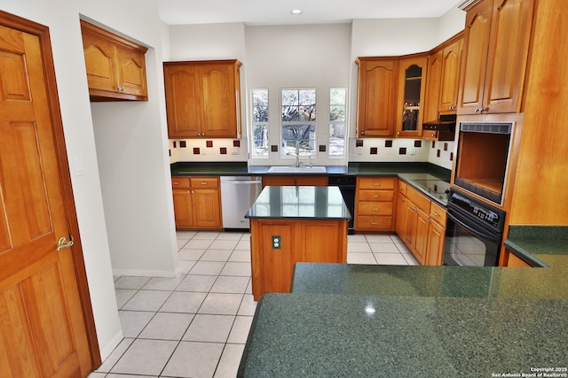 kitchen featuring a center island, brown cabinets, black appliances, dark countertops, and glass insert cabinets