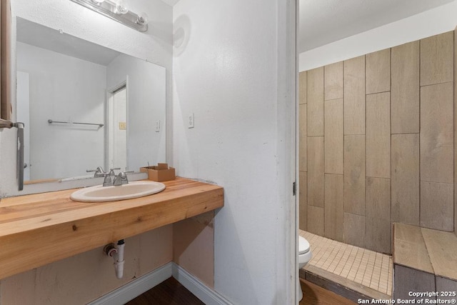 full bathroom featuring a tile shower, a sink, toilet, and baseboards