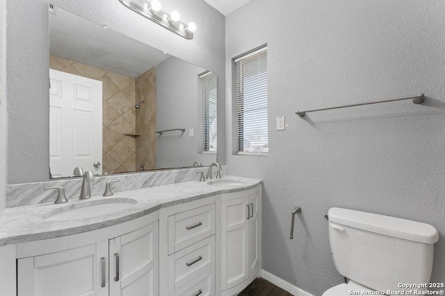 bathroom featuring double vanity, toilet, a sink, and a textured wall