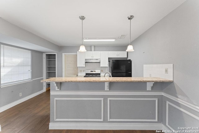 kitchen with a kitchen breakfast bar, freestanding refrigerator, a peninsula, stainless steel stove, and under cabinet range hood