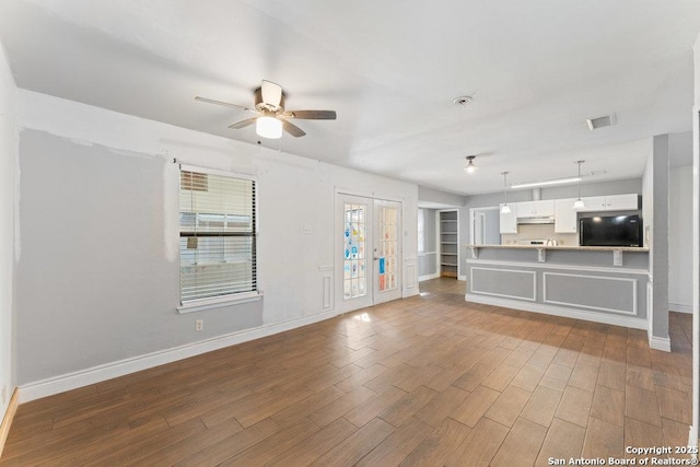 unfurnished living room featuring a ceiling fan, visible vents, baseboards, and wood finished floors