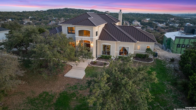 back of house at dusk featuring a standing seam roof, a chimney, and metal roof