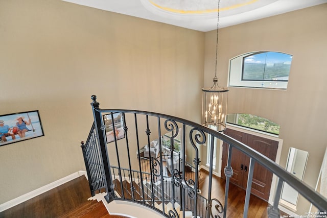 staircase with wood finished floors, baseboards, and an inviting chandelier