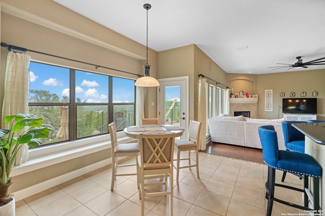 dining space featuring light tile patterned floors, a fireplace, baseboards, and a ceiling fan