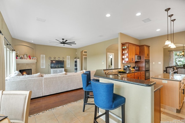 kitchen with pendant lighting, a breakfast bar area, open shelves, open floor plan, and a kitchen island with sink