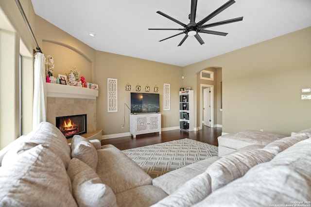 living area with baseboards, arched walkways, a tile fireplace, ceiling fan, and dark wood-style flooring