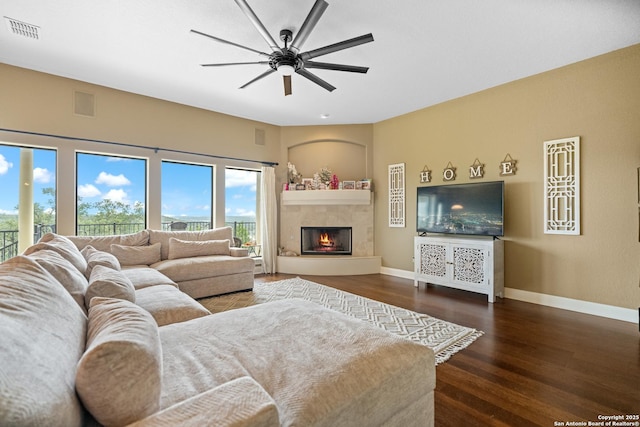 living room featuring baseboards, visible vents, a glass covered fireplace, ceiling fan, and dark wood-type flooring