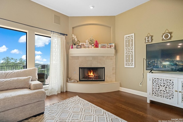 living room featuring visible vents, baseboards, wood finished floors, and a tile fireplace