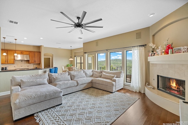 living room with ceiling fan, a fireplace, visible vents, and dark wood finished floors