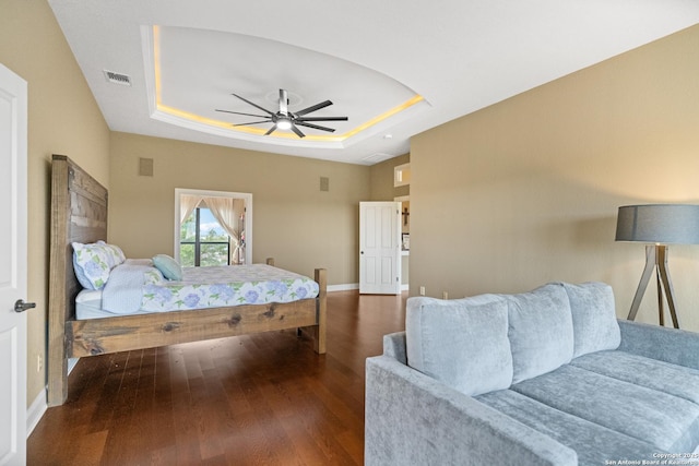 bedroom with visible vents, dark wood finished floors, baseboards, ceiling fan, and a tray ceiling