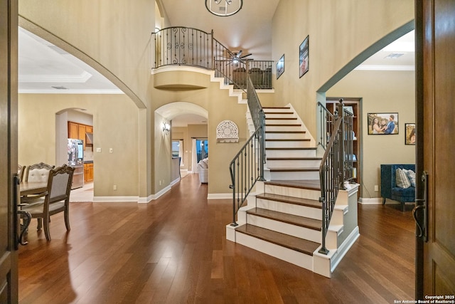 entryway with arched walkways, dark wood finished floors, and crown molding