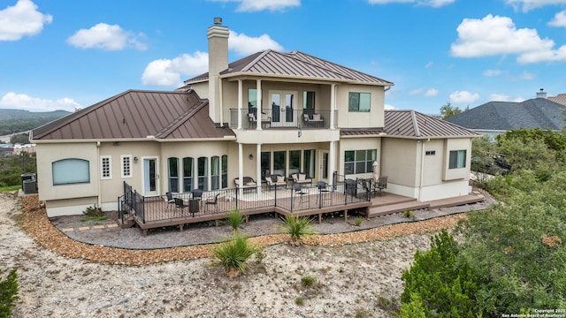 back of house featuring a balcony, a chimney, metal roof, a standing seam roof, and a wooden deck