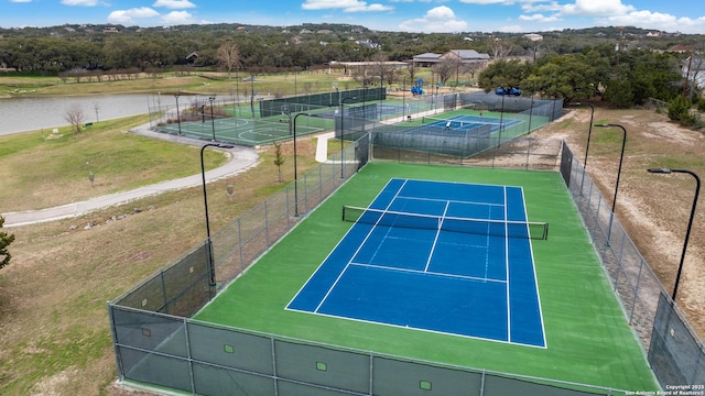 view of tennis court with a water view and fence