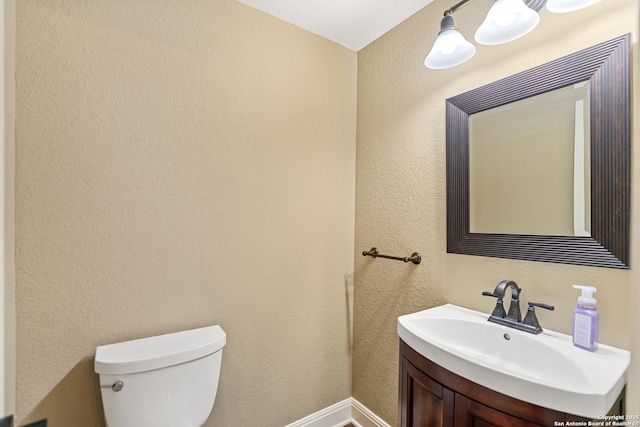 half bath featuring a textured wall, vanity, and toilet