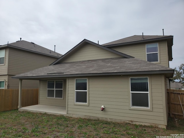 back of property with a shingled roof, a patio area, and fence