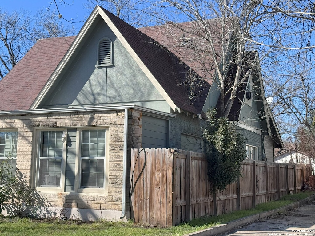 view of side of property with fence and roof with shingles