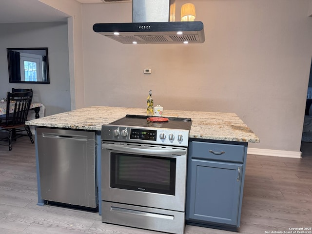 kitchen featuring baseboards, island exhaust hood, appliances with stainless steel finishes, light wood finished floors, and blue cabinets