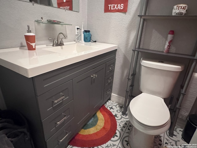 half bathroom featuring toilet, vanity, a textured wall, and baseboards