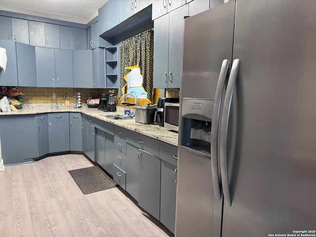 kitchen with light wood-type flooring, open shelves, appliances with stainless steel finishes, a sink, and backsplash