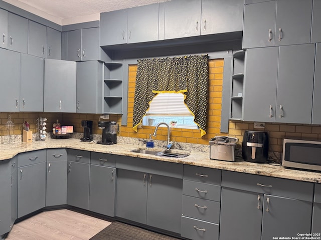 kitchen featuring open shelves, stainless steel microwave, a sink, decorative backsplash, and gray cabinetry