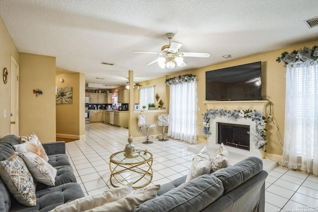 living area featuring a ceiling fan, visible vents, light tile patterned flooring, and a stone fireplace