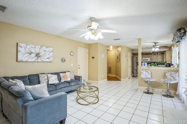 living area featuring light tile patterned floors, ceiling fan, visible vents, and a textured ceiling