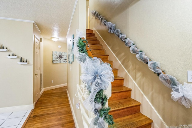 stairs featuring crown molding, a textured ceiling, baseboards, and wood finished floors