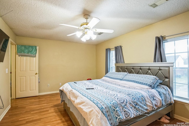 bedroom featuring baseboards, visible vents, a textured ceiling, and light wood finished floors