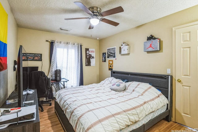 bedroom with a ceiling fan, visible vents, a textured ceiling, and wood finished floors