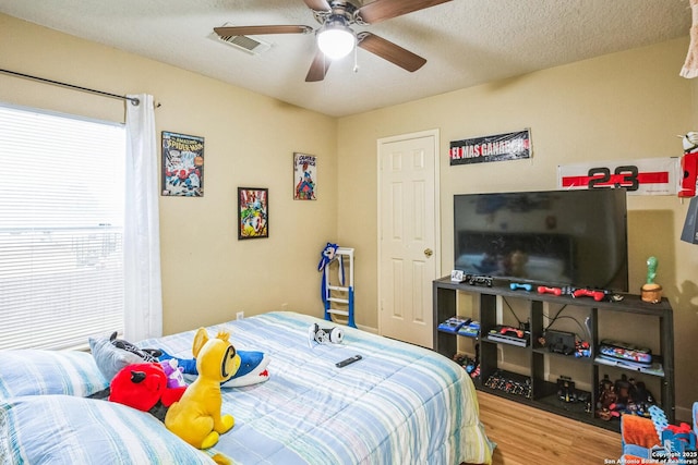 bedroom featuring a ceiling fan, a textured ceiling, visible vents, and wood finished floors