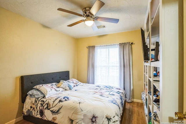 bedroom featuring baseboards, visible vents, a ceiling fan, dark wood-style floors, and a textured ceiling