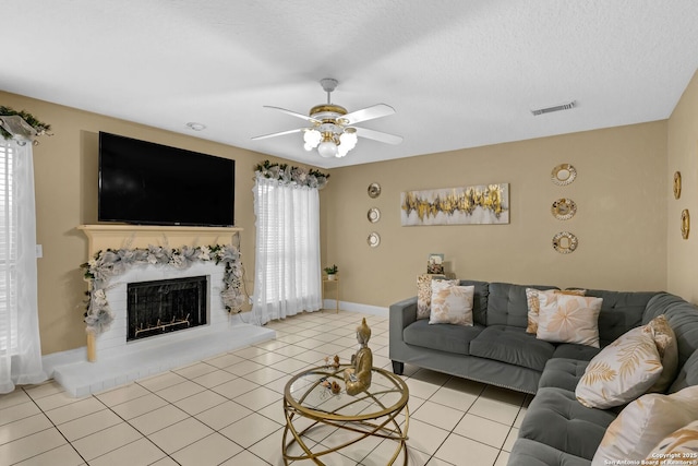 living area with light tile patterned floors, visible vents, a fireplace with raised hearth, ceiling fan, and baseboards