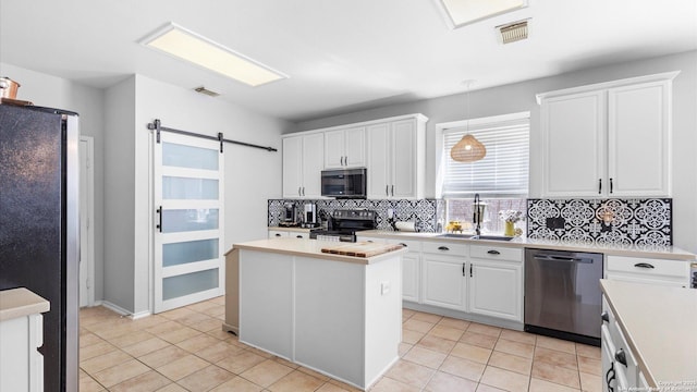 kitchen with a barn door, appliances with stainless steel finishes, a center island, light countertops, and white cabinetry