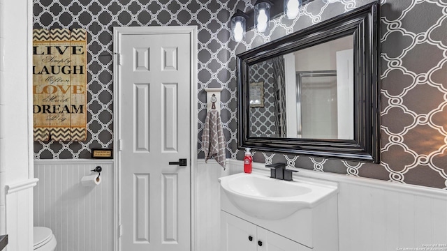 bathroom with a wainscoted wall, toilet, and wallpapered walls