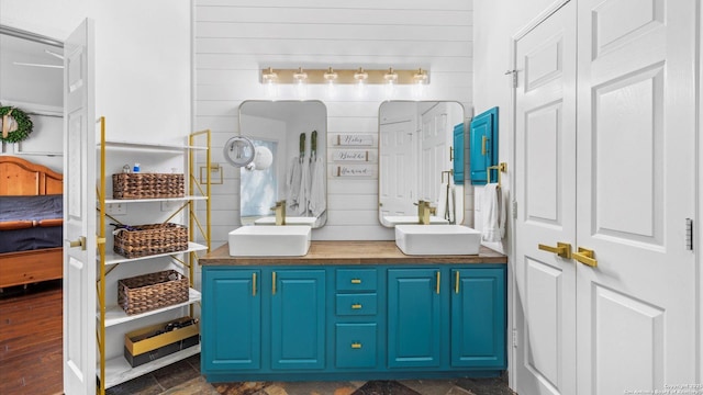 full bath with double vanity, wooden walls, and a sink