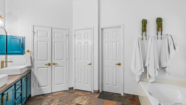 full bathroom with a bathtub, double vanity, a closet, stone tile flooring, and a sink