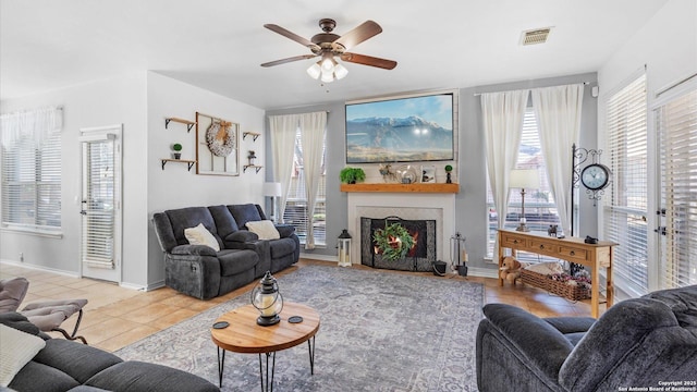 living area featuring a fireplace, light tile patterned floors, visible vents, ceiling fan, and baseboards