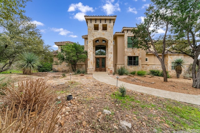 mediterranean / spanish house with stone siding, french doors, a tiled roof, and stucco siding